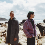 Portrait des deux musiciens réalisé sur les rochers en bord de mer, tous les deux regardent vers l'horizon, ils sont côté à côté presque de dos à dos